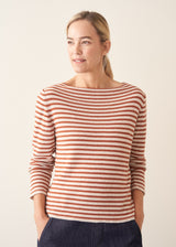 Woman wearing burnt orange and oatmeal striped fine knit sweater with blue denim trousers