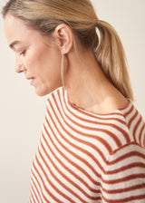 Woman wearing burnt orange and oatmeal striped fine knit sweater with blue denim trousers