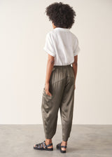 Woman wearing a white linen short sleeve shirt and khaki green satin cargo trousers against a plain background