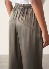 Woman wearing a white linen short sleeve shirt and khaki green satin cargo trousers against a plain background