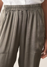Woman wearing a white linen short sleeve shirt and khaki green satin cargo trousers against a plain background