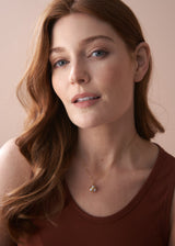 Woman wearing a cluster pearl necklace on delicate gold chain, with a terracotta tank top
