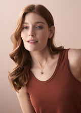 Woman wearing a cluster pearl necklace on delicate gold chain, paired with a terracotta tank top