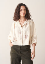 Woman wearing light cream devoree jacquard textured shirt and green trousers