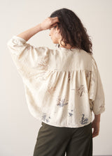 Woman wearing light cream devoree jacquard textured shirt and green trousers