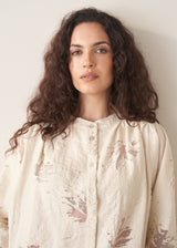 Woman wearing light cream devoree jacquard textured shirt and green trousers