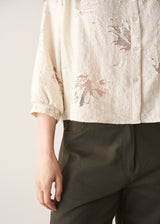 Woman wearing light cream devoree jacquard textured shirt and green trousers