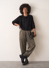 Woman wearing a black vintage-style jacquard blouse with khaki satin trousers on a neutral background