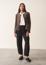 A woman wearing a matching leopard-print jacket and trousers set with a white shirt and a black clutch bag.