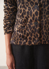 A woman wearing a matching leopard-print jacket and trousers set with a white shirt and a black clutch bag.