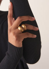 Close up of women wearing a bold, eye-catching ring with a chunky double-band design and brushed gold finish, on a beige background