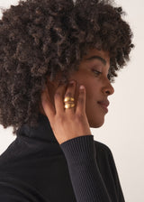 Woman wearing a bold, eye-catching ring with a chunky double-band design and brushed gold finish, on a beige background