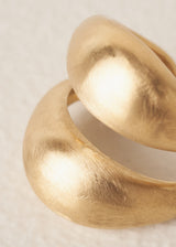 Close up of bold, eye-catching ring with a chunky double-band design and brushed gold finish, on a beige background