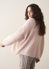 Woman wearing an oversized blush pink chunky knit cardigan with checked trousers