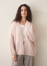 Woman wearing an oversized blush pink chunky knit cardigan with checked trousers