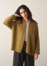 Woman wearing an olive green chunky knitted cardigan against a plain background