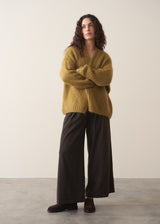 Woman wearing an olive green chunky knitted cardigan with wide leg trousers against a plain background