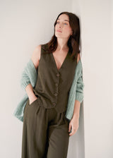 Woman wearing a linen blend waistcoat and trousers with a chunky knit mint cardigan, against a beige background