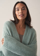 A woman model wears a mint green chunky knit cardigan with a striped top against a beige background