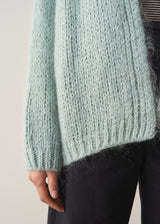 Woman wearing a mint green chunky knit cardigan with a striped top and black wide leg trousers