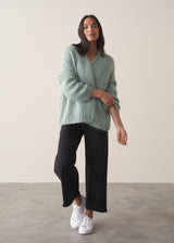 Woman wearing a mint green chunky knit cardigan with a striped top and black wide leg trousers