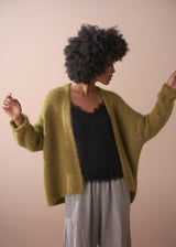 Person wearing olive green chunky cardigan, black satin cami and striped trousers on neutral background.