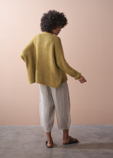 Woman wearing an olive green chunky cardigan and striped trousers, facing a neutral background.