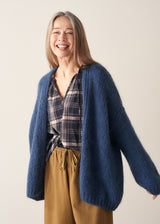 A woman wearing a blue chunky knit oversized cardigan with a checked shirt and mustard trousers