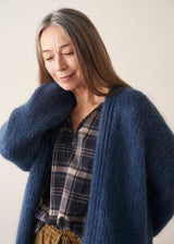 A woman wearing a blue chunky knit oversized cardigan with a checked shirt and mustard trousers