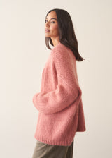 Woman wearing rose pink chunky knit cardigan with soft green trousers and a white blouse