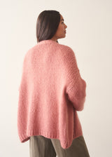 Woman wearing rose pink chunky knit cardigan with soft green trousers and a white blouse
