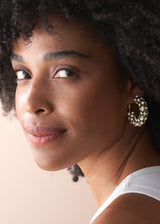 Woman wearing chunky crystal adorned hoop earrings with white top