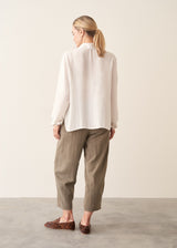 A woman wearing a vintage white long-sleeve button-up sheer blouse and light green khaki trousers.