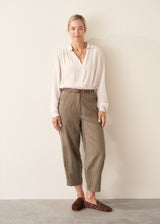 A woman wearing a vintage white long-sleeve button-up sheer blouse and light green khaki trousers.