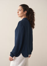 Woman wearing a dark teal blouse and white barrel leg jeans