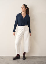 Woman wearing a dark teal blouse and white barrel leg jeans with brown loafers