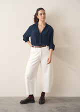 Woman wearing a dark teal blouse and white barrel leg jeans and brown loafers