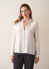 Woman wearing a white silk shirt and dark jeans against a plain background