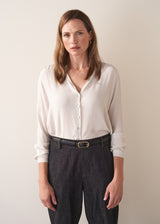 Woman wearing a white silk shirt and dark jeans against a plain background