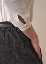 Woman wearing a white silk shirt and dark jeans against a plain background