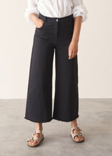 Woman wearing white broderie anglaise top and black cotton wide leg trousers with sandals