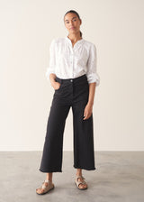 Woman wearing white broderie anglaise top and black cotton wide leg trousers with sandals