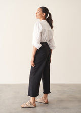 Woman wearing white broderie anglaise top and black cotton wide leg trousers with sandals