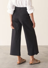 Woman wearing white broderie anglaise top and black cotton wide leg trousers with sandals