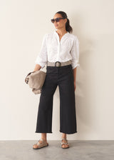 Woman wearing white broderie anglaise top and black cotton wide leg trousers with sandals