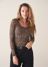 A woman wearing a form fitting long sleeve leopard print top with a grey cardigan and black trousers