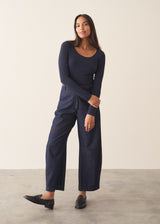 A woman wearing a dark blue long sleeve cashmere blend layering top with dark blue jeans and stud loafers.