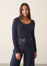 A woman wearing a dark blue long sleeve cashmere blend layering top with dark blue jeans and stud loafers.