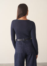 A woman wearing a dark blue long sleeve cashmere blend layering top with dark blue jeans and stud loafers.