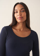 A woman wearing a dark blue long sleeve cashmere blend layering top with dark blue jeans and stud loafers.